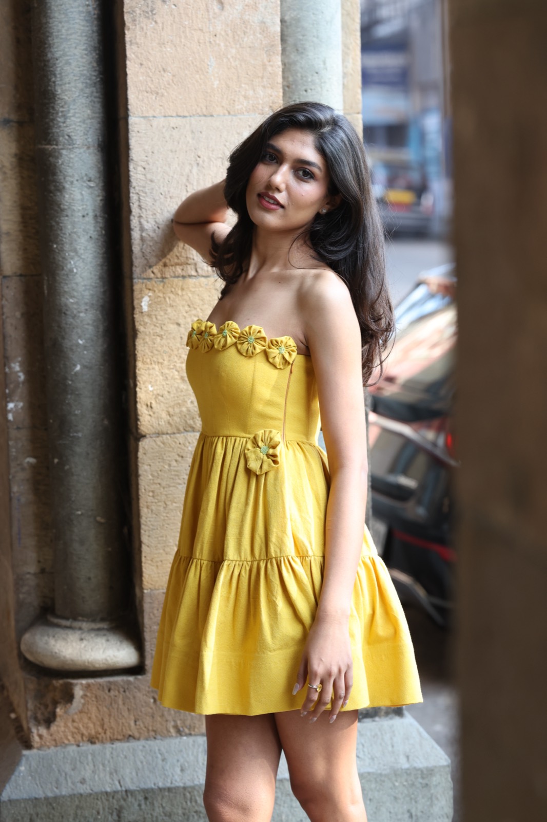 Berry Butter — yellow tiered mini dress with a rosette-trimmed bodice, against a stone colonnade