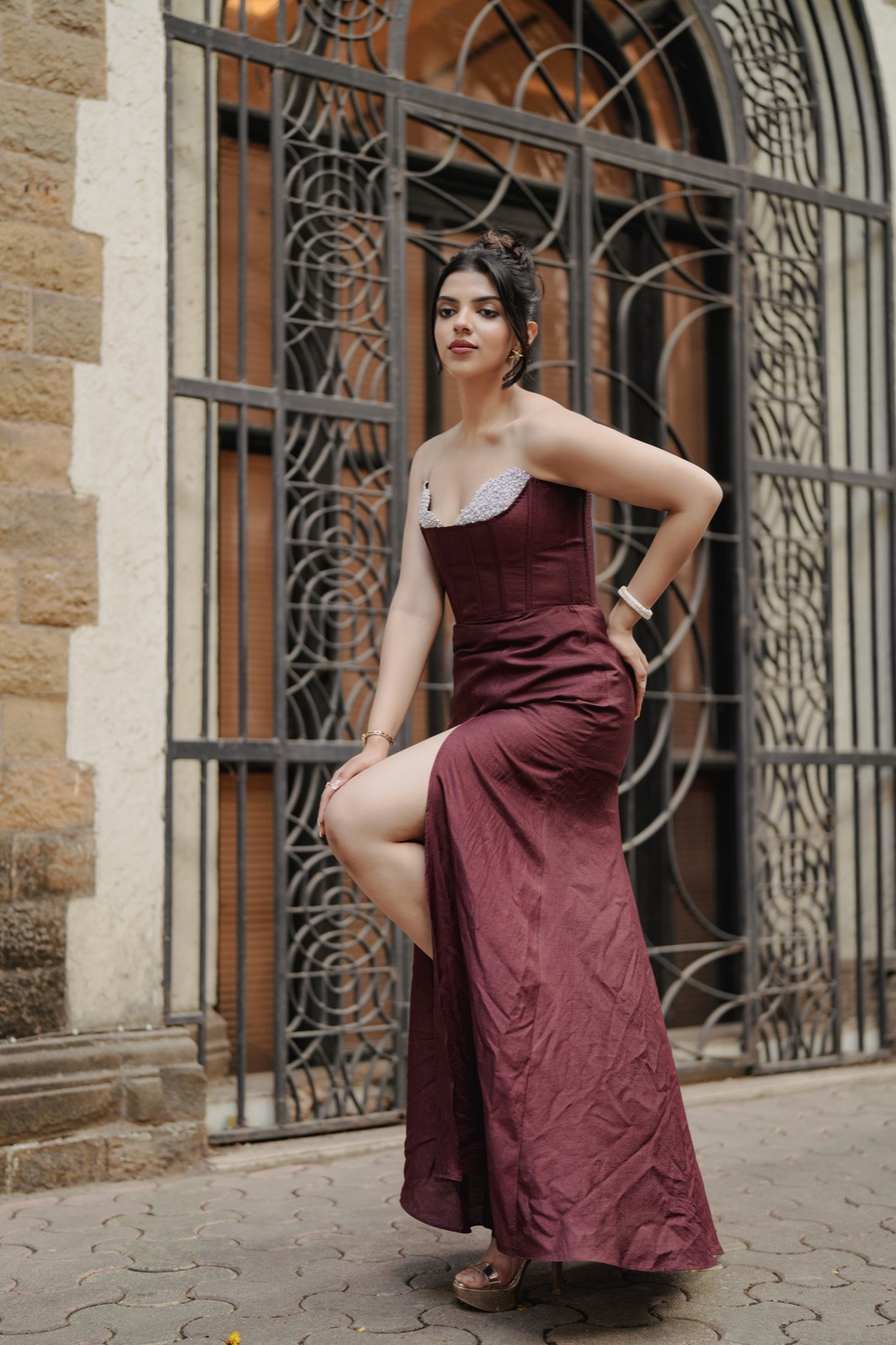 Claret Column — standing against sandstone with a hand at her hip