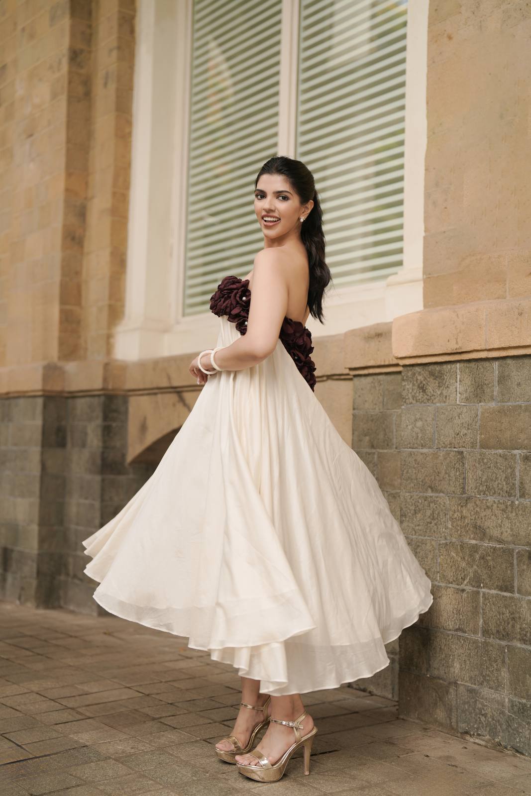 Rustic Roses Midi Dress — Ivory gown with a Bordeaux rosette bodice, against a stone facade in Mumbai